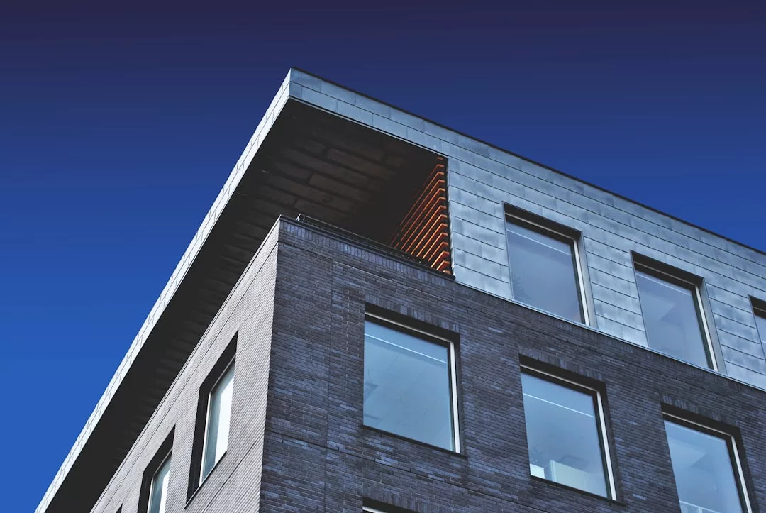 A modern real estate building with brick and metal cladding, featuring large square windows, set against a clear blue sky.