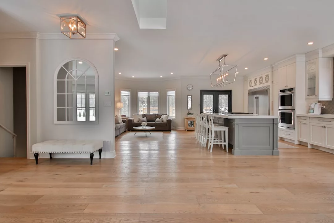 Spacious modern kitchen and living room, perfect for real estate seekers, featuring light wood flooring, white cabinetry, a large island, and a cozy sitting area by bay windows.