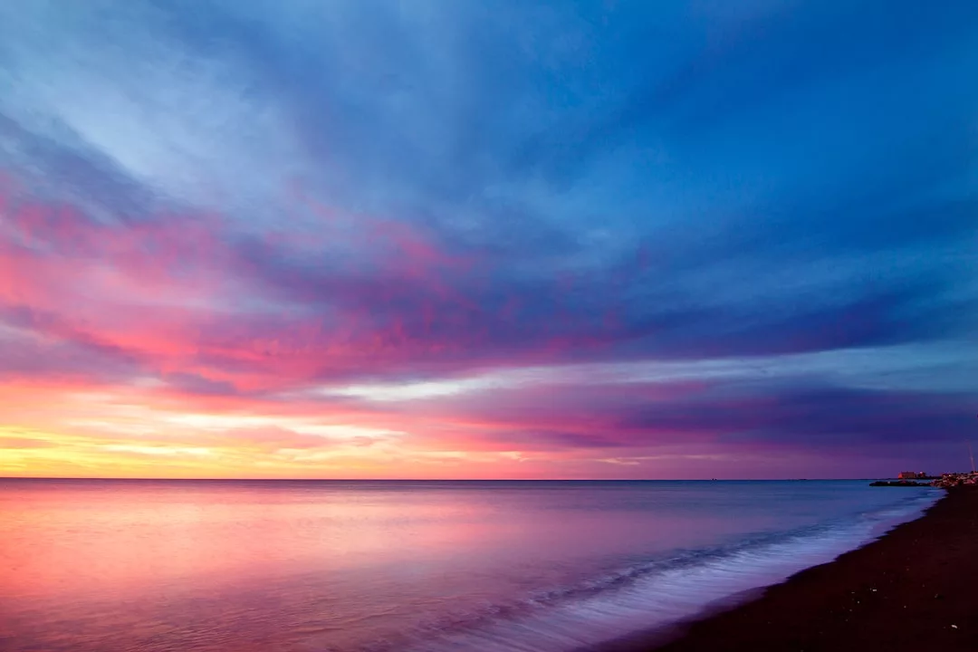 A calm beach at sunset with vibrant pink, purple, and blue clouds reflecting on the water—an idyllic scene perfect for showcasing prime real estate by the shore.