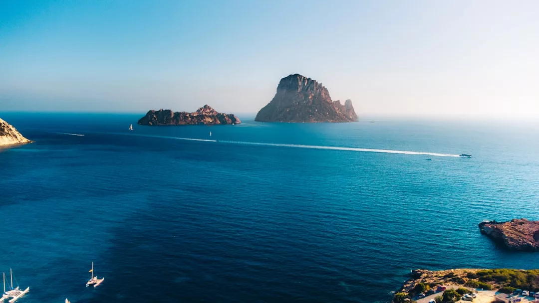 A clear blue sea with several boats, rocky islands in the distance, and a hazy sky above—an idyllic setting perfect for prime real estate opportunities.