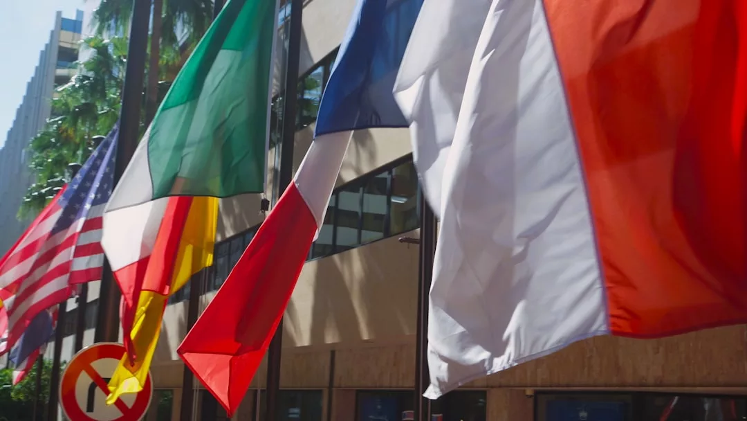 Several national flags, including those of the United States, Italy, France, and Belgium, are displayed outside a modern real estate building.