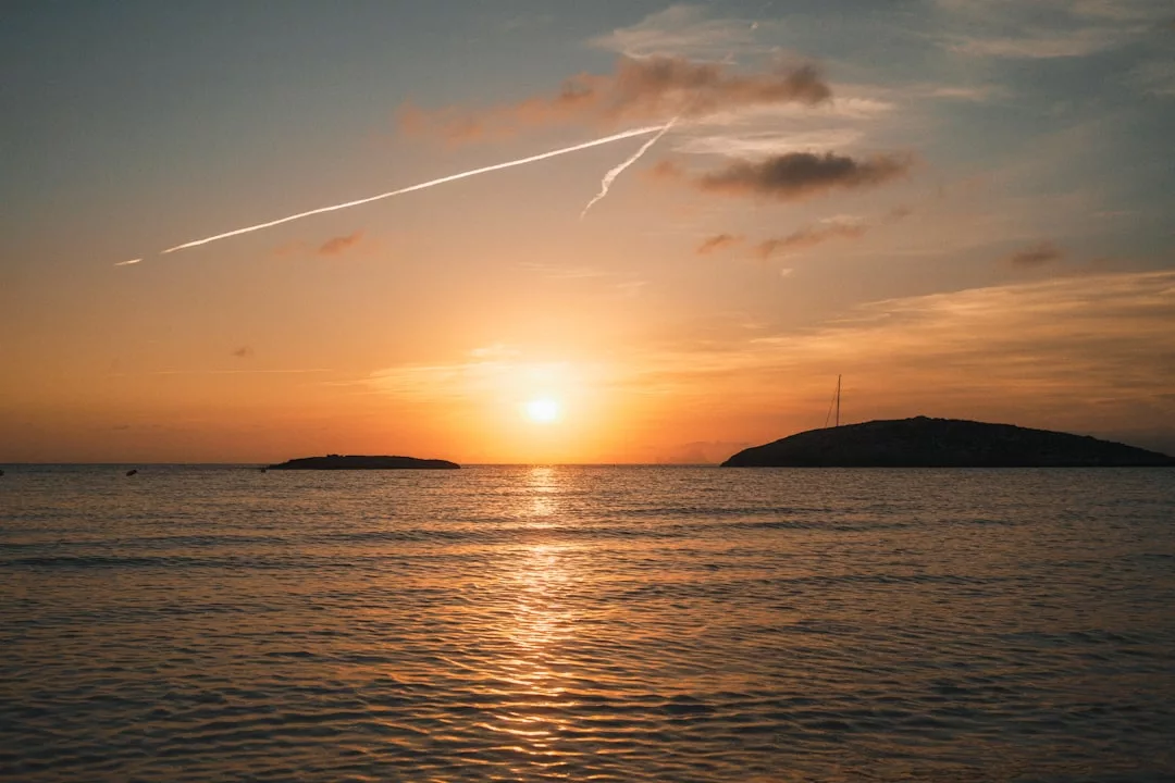 Sunset over a calm sea with two small islands on the horizon and a vapor trail crossing the sky—an inspiring view that makes this Real Estate location truly exceptional.