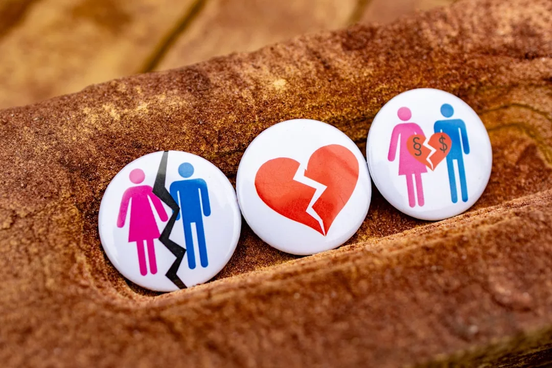Three pins on a textured surface: one shows a couple split by a crack, one displays a broken heart, and one depicts a couple with a Real Estate court document separating them.