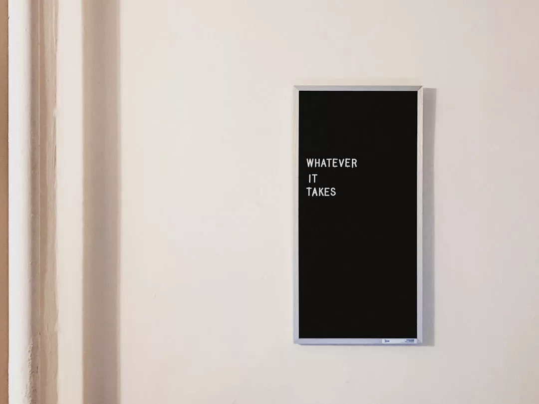 A black rectangular sign on a white wall displays the phrase "WHATEVER IT TAKES" in white capital letters—a fitting motto for those driven by Real Estate success.