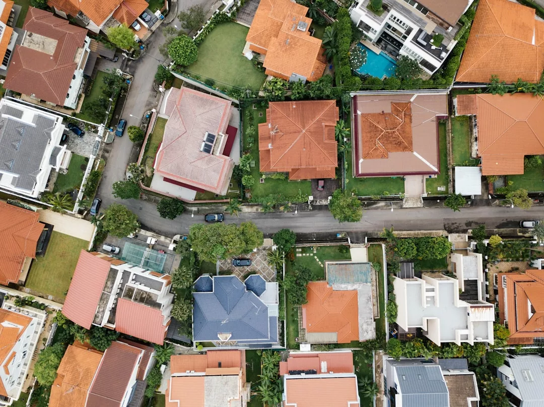 Aerial view of a residential neighborhood showcasing real estate with houses featuring red and gray roofs, green lawns, trees, and a road running through the area.
