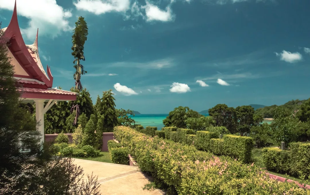 A landscaped garden with lush greenery and a traditional structure overlooks a turquoise sea under a partly cloudy sky, offering stunning real estate views.