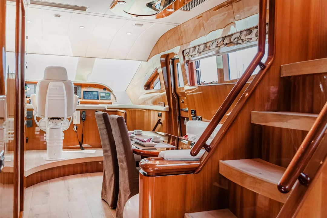 Interior of a yacht featuring wooden stairs, a dining table with chairs, and a captain's chair at the helm with navigation equipment—an exceptional showcase of luxury real estate on the water.