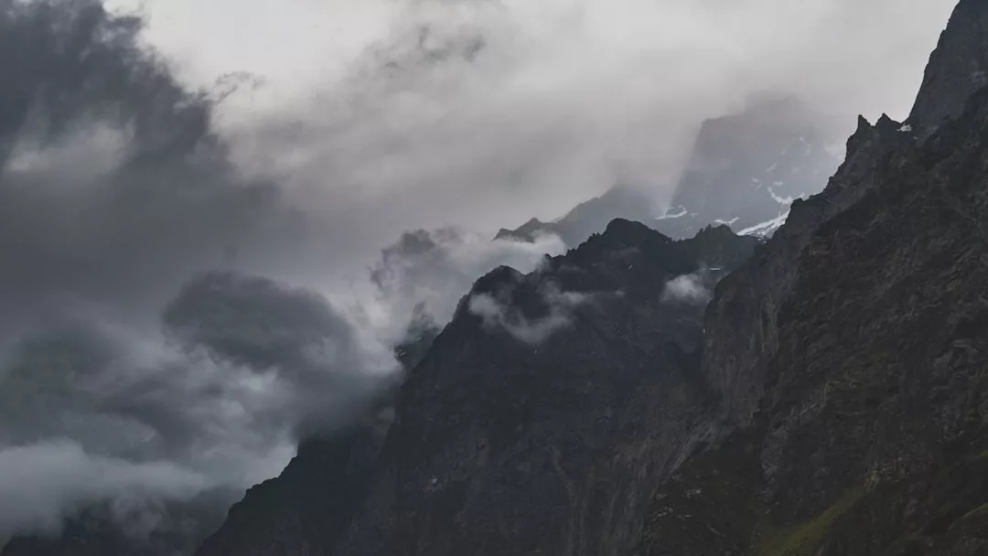 Dark, jagged mountain peaks are partially obscured by thick clouds and mist, creating a dramatic landscape that showcases the unique allure of real estate nestled in nature's most striking scenery.