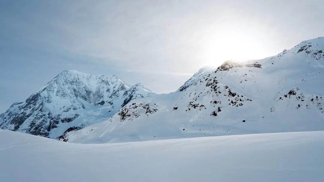 Snow-covered mountains under a clear sky with the sun partially hidden behind a peak, casting light over the winter landscape—a breathtaking view perfect for premium real estate opportunities.