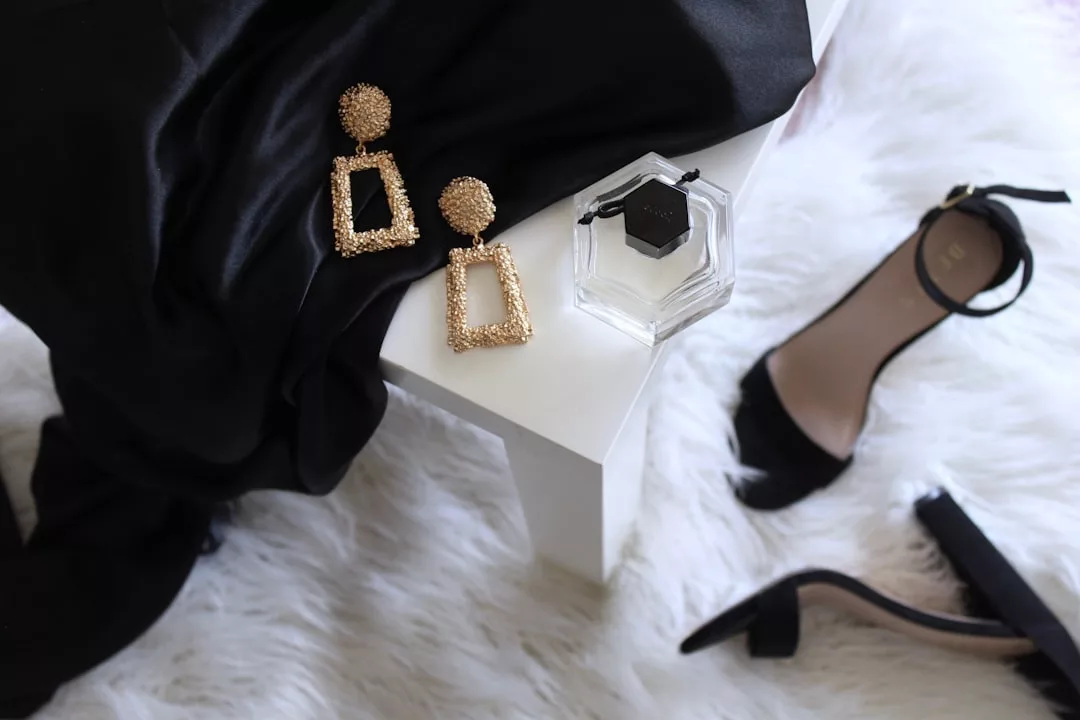 A pair of gold geometric earrings, a hexagonal perfume bottle, and black high-heeled sandals are artfully arranged on a white furry rug—an elegant scene that adds luxury and style to any real estate listing.