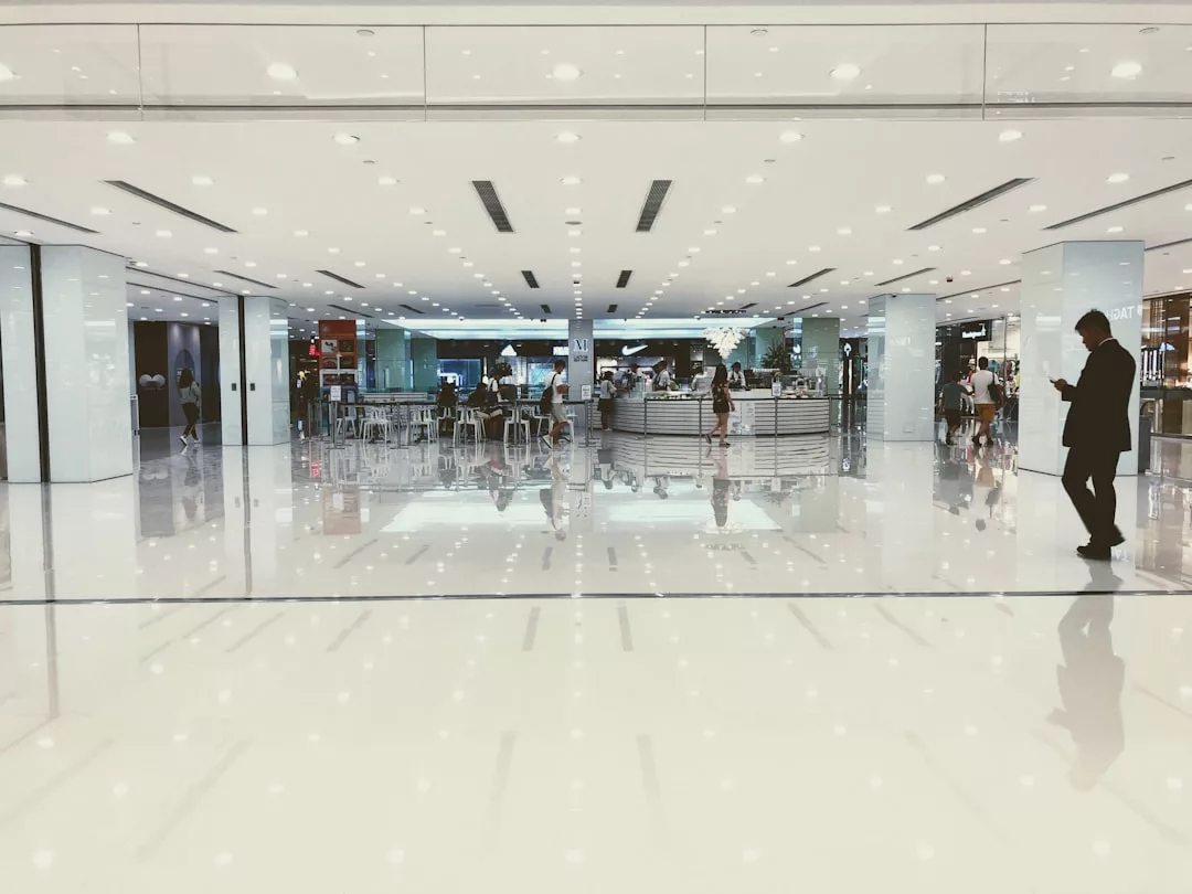 Spacious, brightly lit mall interior with shiny white floors, scattered tables, and people walking or sitting near a central circular counter—an inviting real estate opportunity in a vibrant commercial setting.