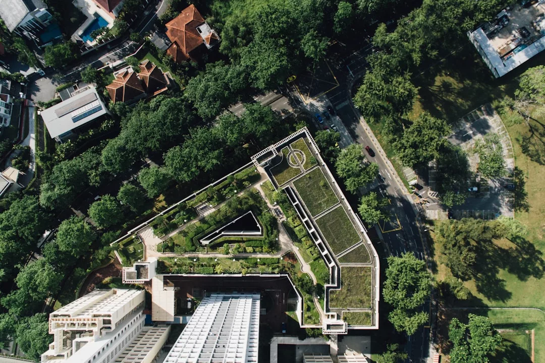 Aerial view of a city building with a rooftop garden, surrounded by trees, roads, and other real estate properties.