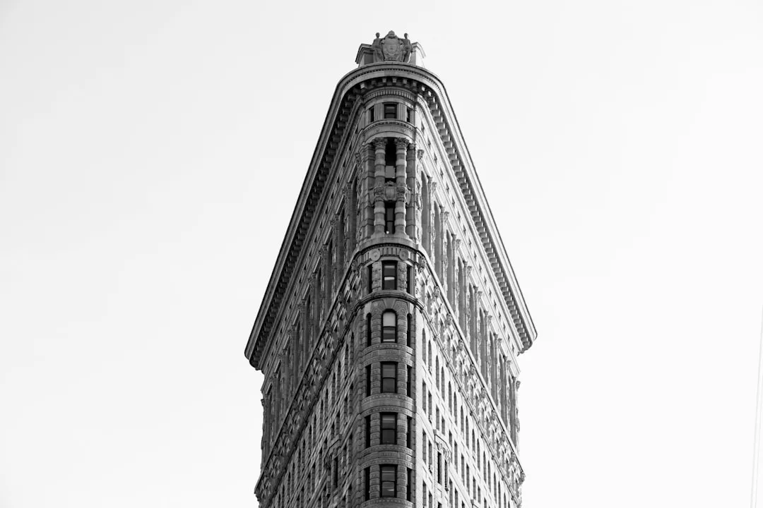 Black and white photo of the Flatiron Building in New York City, capturing its distinctive triangular shape from a low angle—a timeless icon in real estate set against a plain sky.
