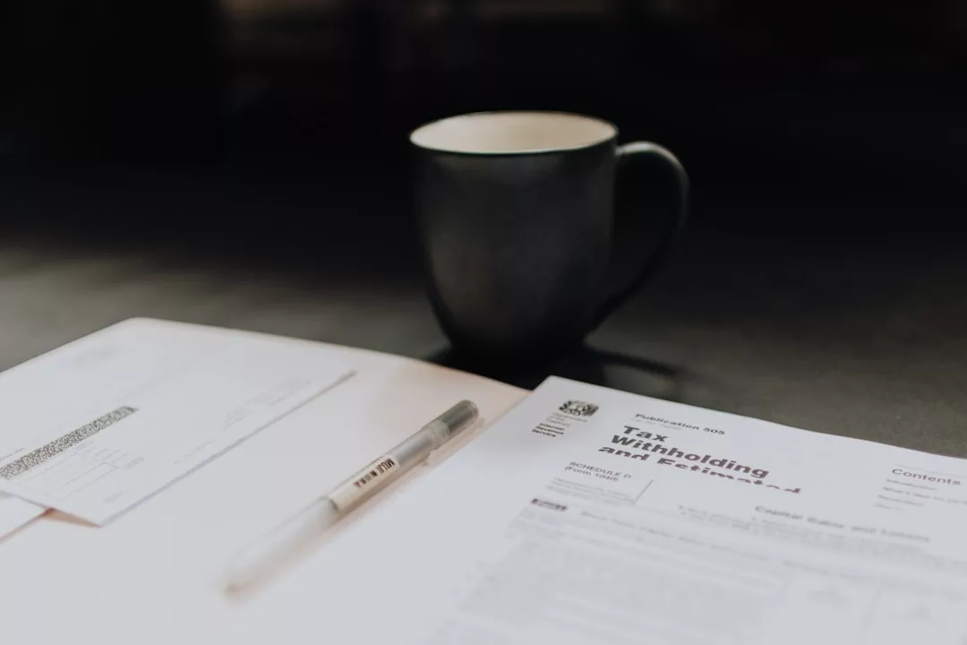 A pen, a tax withholding form, an envelope, and a coffee mug are placed on a table—tools often found in the world of real estate.