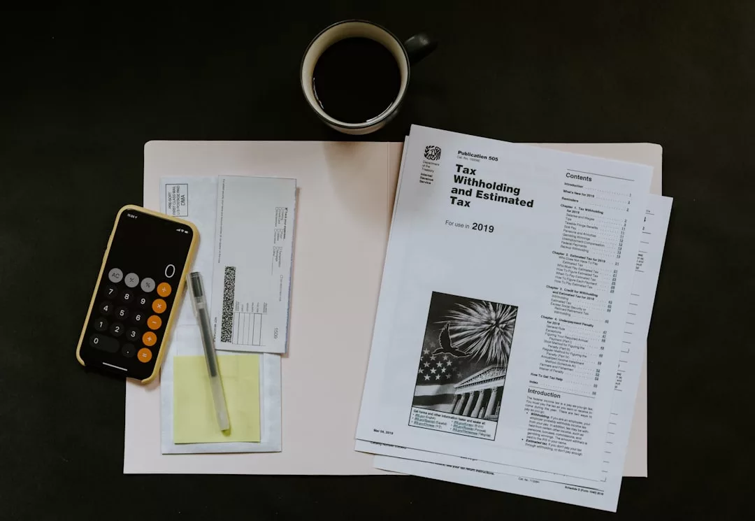 A folder with tax documents, a calculator, a pen, real estate papers, some envelopes, and a cup of coffee arranged on a dark surface.