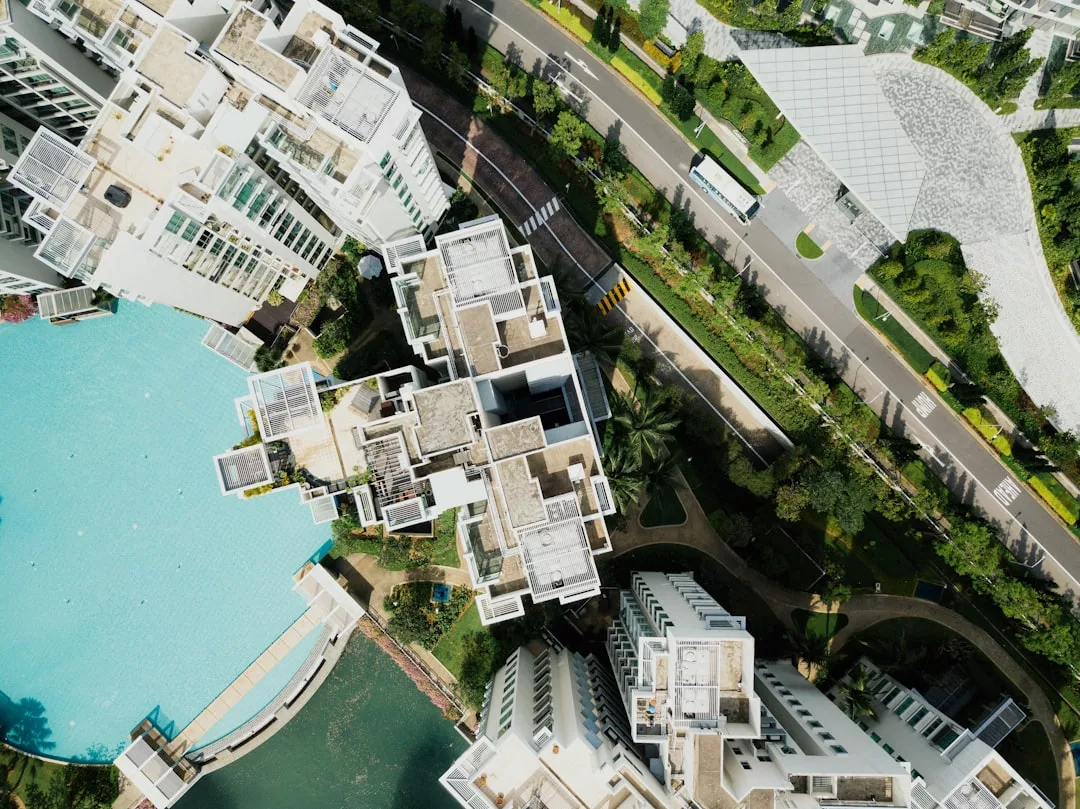 Aerial view of sustainable apartments in Copenhagen, featuring modern buildings with a large swimming pool, adjacent greenery, and a curved road.