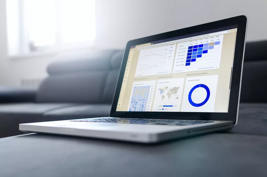A laptop displaying real estate data analytics dashboards, including charts, graphs, and maps, sits on a gray couch in a modern living room.