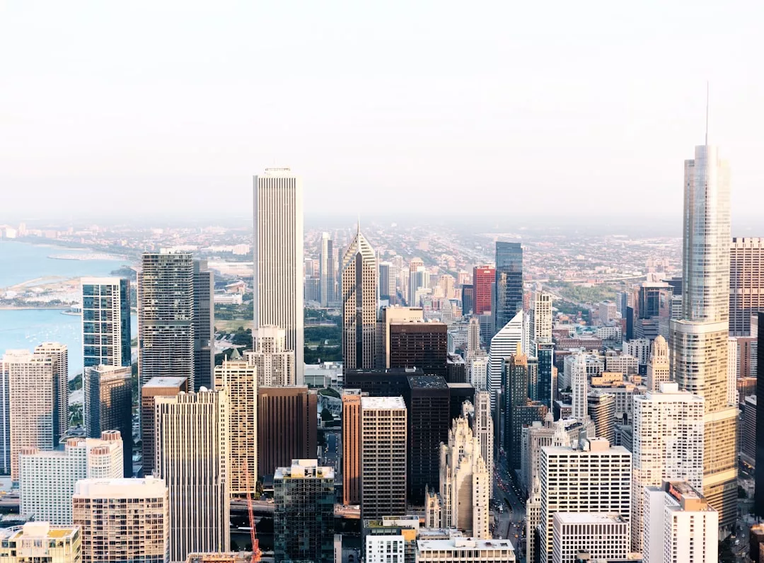 Aerial view of a city skyline highlighting tall skyscrapers, prime real estate developments, a body of water on the left, and a sprawling urban landscape in the background.