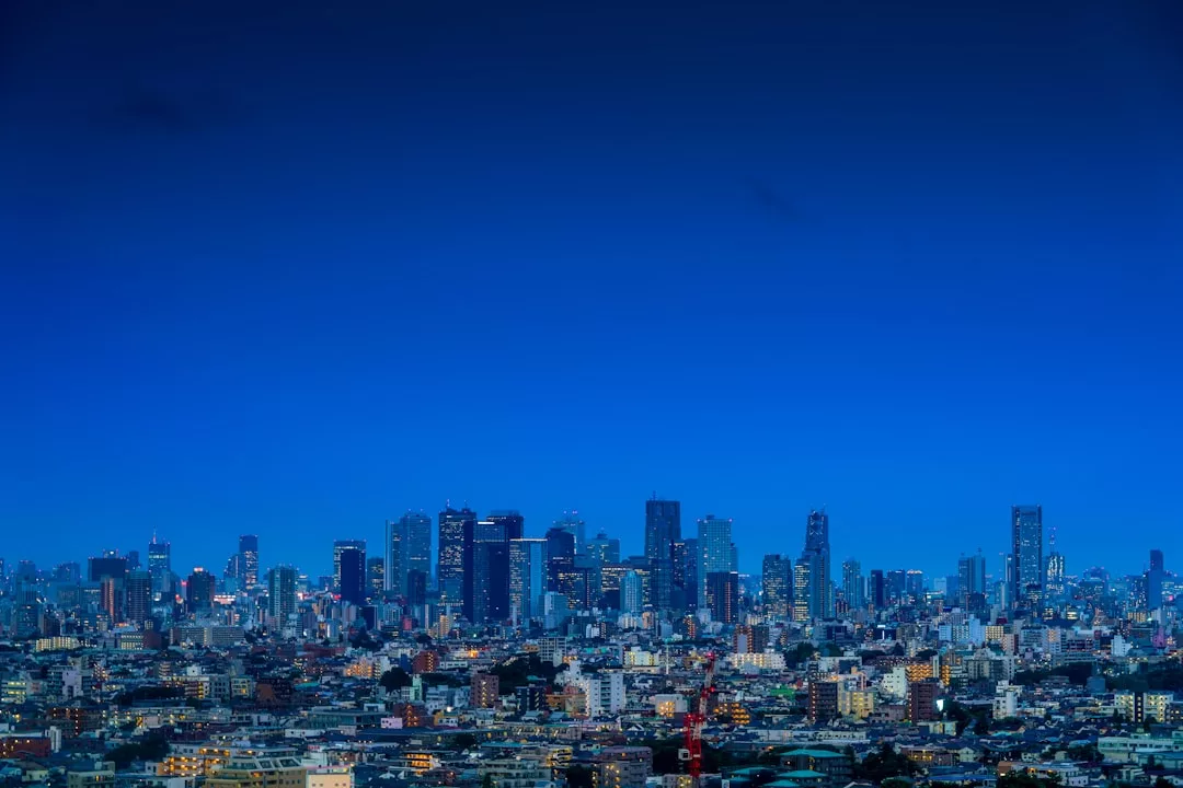 City skyline of Oslo with numerous high-rise buildings under a clear, deep blue evening sky. Recent infrastructure developments are evident, with residential and commercial buildings visible in the foreground.