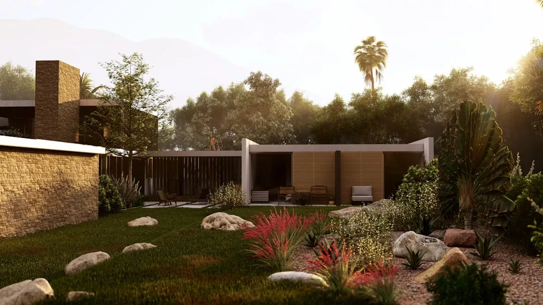 Modern real estate featuring large windows, a shaded patio, and a landscaped yard with rocks, green grass, and ornamental plants—all surrounded by trees in warm sunlight.