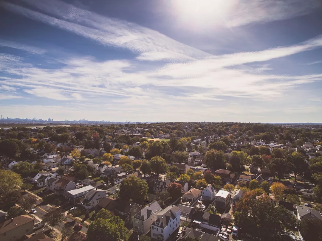 Aerial view of a suburban neighborhood, highlighting houses and trees, with distant skyline under a partly cloudy sky and bright sunlight—ideal for showcasing prime real estate opportunities.