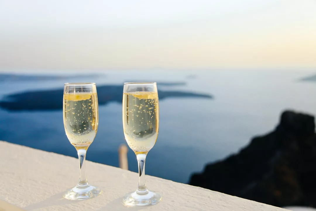 Two glasses of sparkling wine sit on a ledge overlooking a calm sea and distant islands—an idyllic scene that captures the essence of luxurious real estate living.