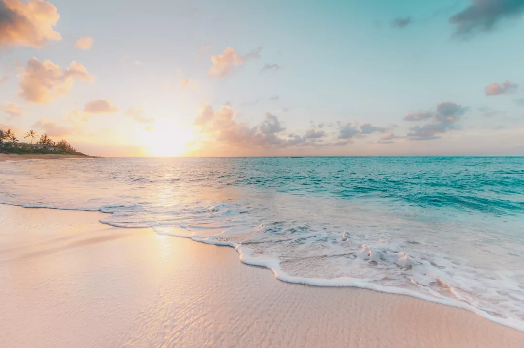 Sunrise over a sandy beach with gentle waves, clear turquoise water, and a partly cloudy sky—this serene view offers the perfect backdrop for your dream real estate investment.