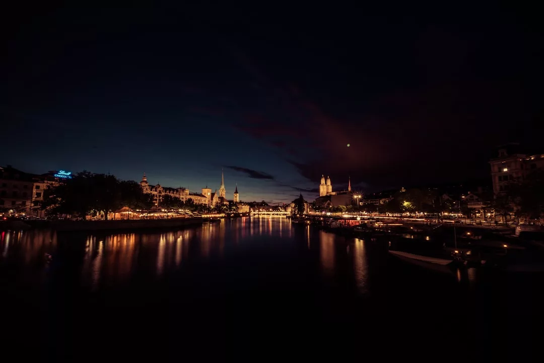 Cityscape at dusk in one of Switzerland's top cities, with illuminated buildings and church spires reflecting on a calm river—an inviting scene for high-yield property investments along the scenic waterfront.