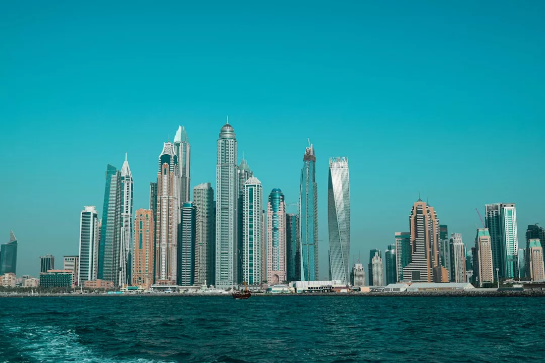 A city skyline with numerous modern skyscrapers along a waterfront, set against a clear blue sky—an impressive hub for premier real estate opportunities.