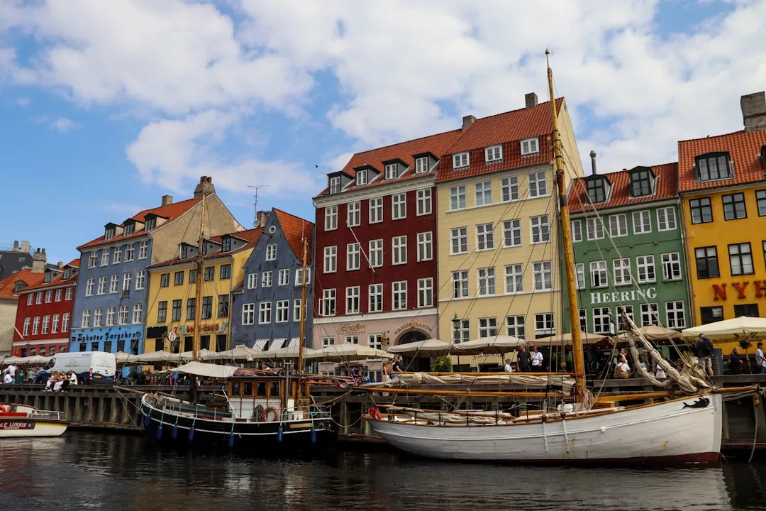 Colorful buildings line Copenhagen’s waterfront, with docked sailboats and people at outdoor cafes. This vibrant scene showcases one of the city's top districts, known for its charm and potential for high-yield property investments.