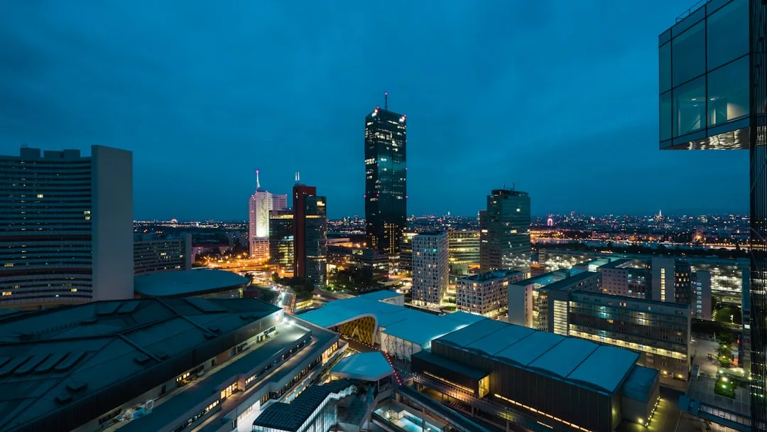 Cityscape at dusk with illuminated skyscrapers and buildings under a dark blue sky, viewed from an elevated perspective, captures Oslo’s stunning cityscape views.