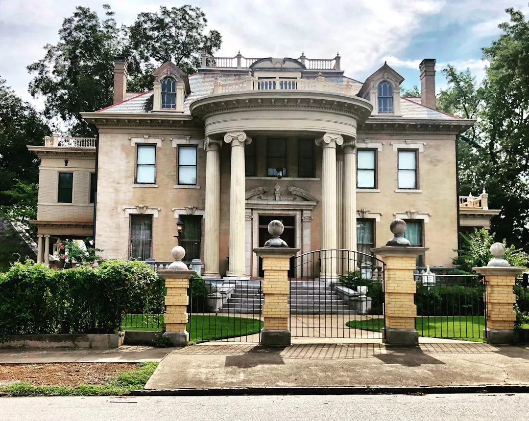 A large historic mansion with tall columns, arched windows, and a gated entrance stands surrounded by trees and greenery—an exceptional real estate opportunity.