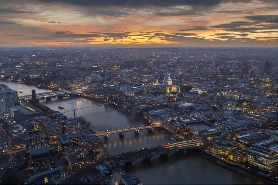 Aerial view of central London at sunset, highlighting the River Thames, several bridges, and St Paul's Cathedral illuminated among city buildings—a stunning scene that showcases the allure of London real estate.
