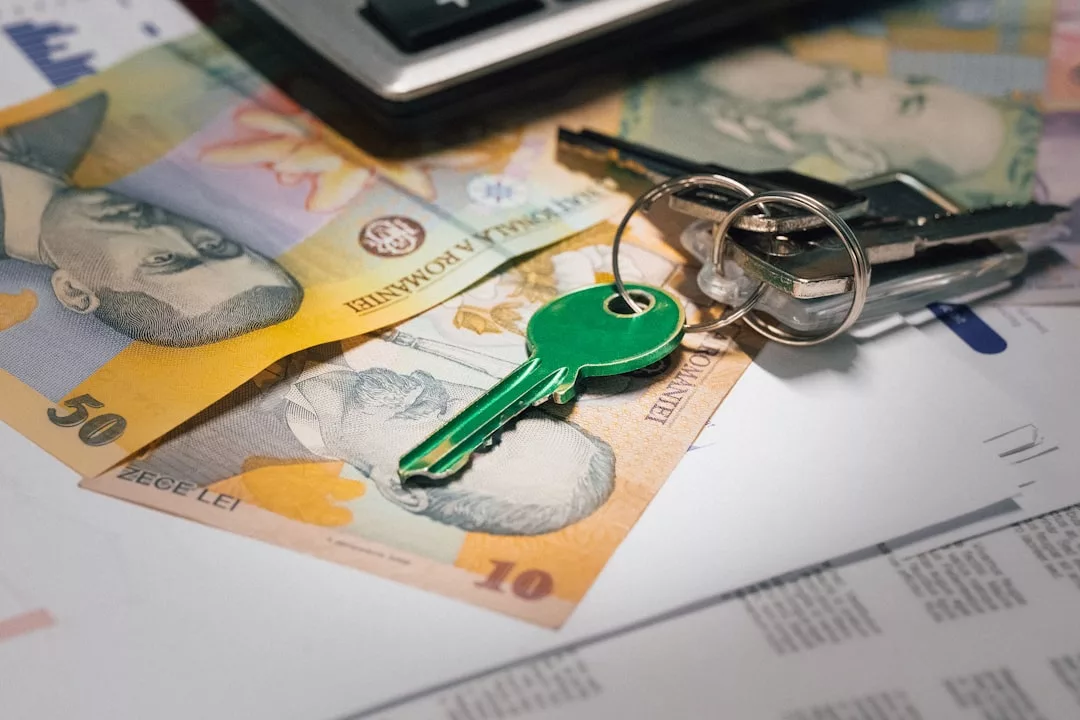 A set of keys with a green key tag and a calculator rest on Romanian banknotes and real estate documents.