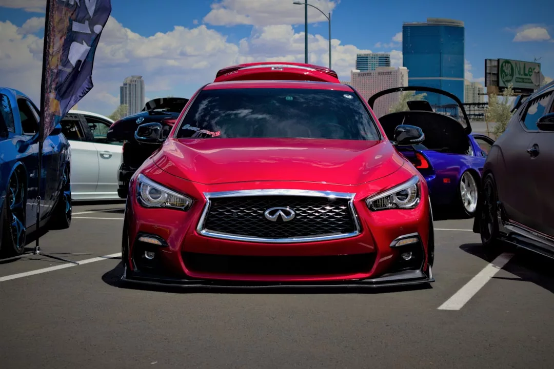 A red Infiniti sedan with a modified body kit, parked at a car show amid custom vehicles on a sunny day—proof that great design isn’t limited to real estate.